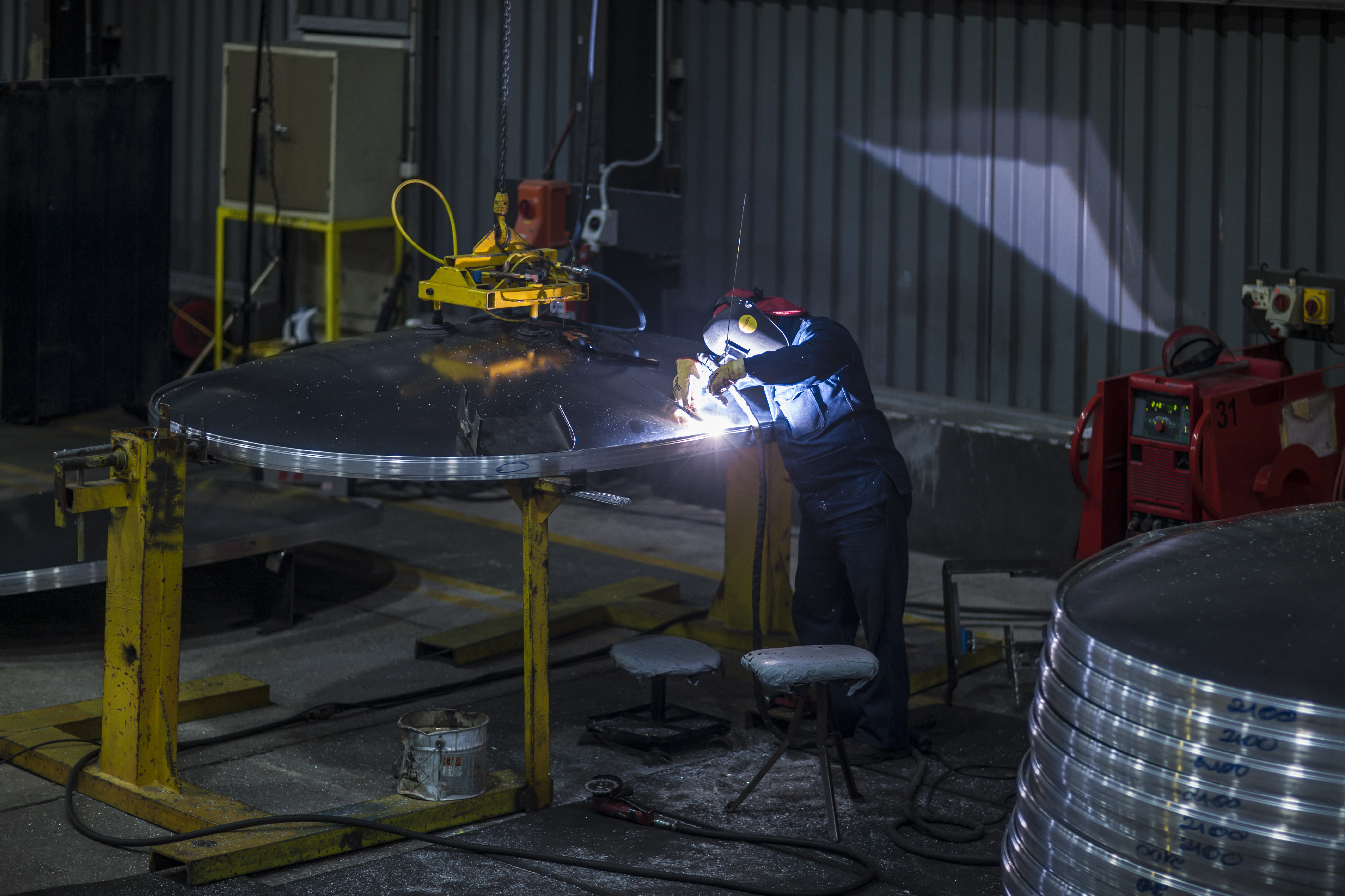 A welder working on a large steel component wearing PPE gear.